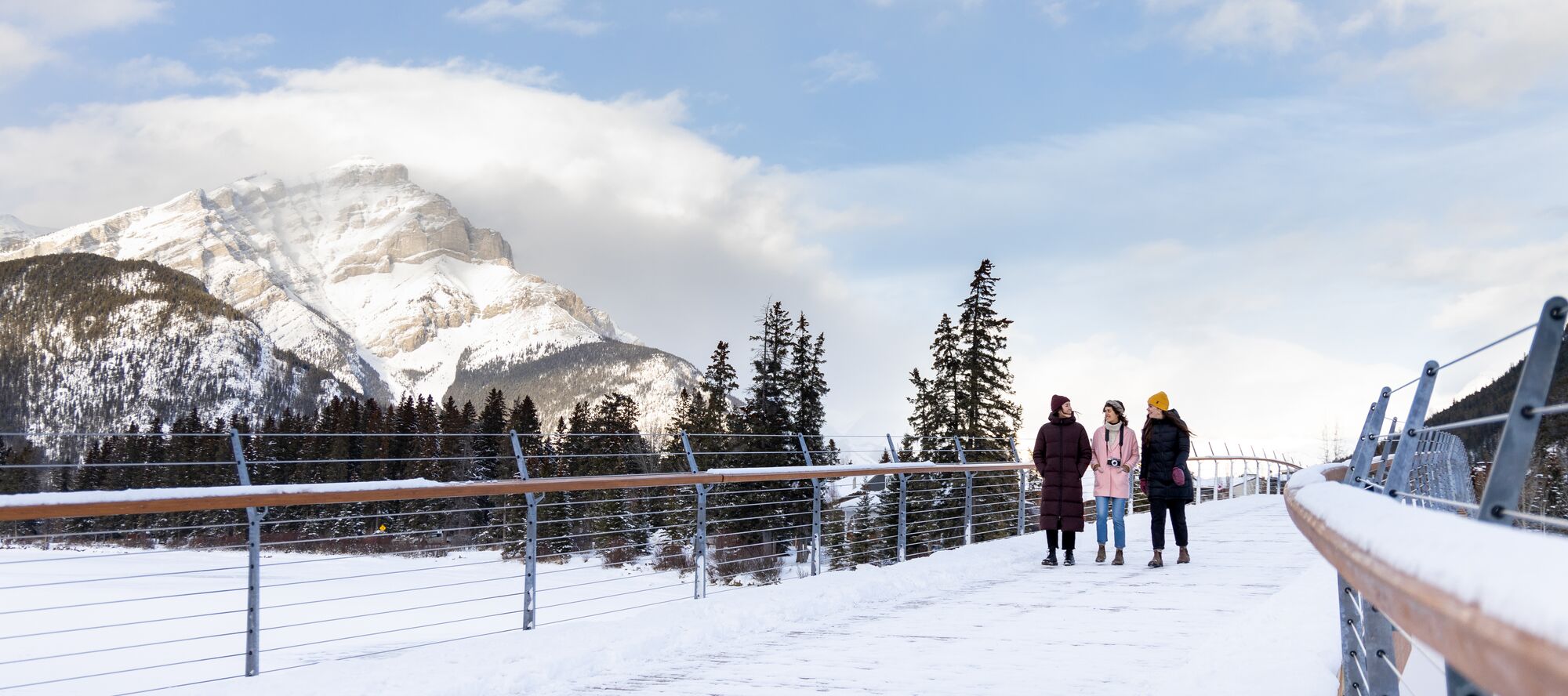 Four friends walk across the Banff Pedestrian Bridge over Bow River in Banff National Park
